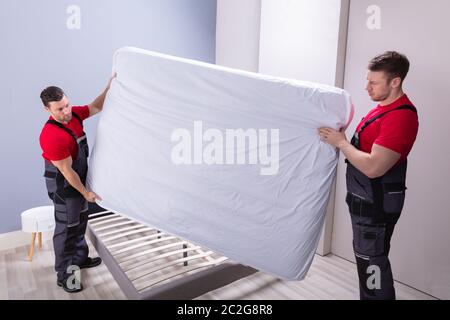 Zwei männliche professionelle Movers in Uniform, die Matratze auf dem Bett in neues Haus Stockfoto