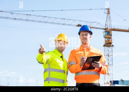 Zwei Jungen männlichen Ingenieure stehen vor der mechanischen Kran auf der Baustelle Stockfoto