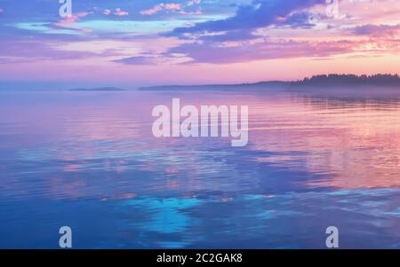 Neblige Seenlandschaft - ruhige Wasseroberfläche des Sees reflektiert lila Himmel mit rosa und blauen Wolken nach Sonnenuntergang. Weiße Nächte Saison in der Republik Kare Stockfoto