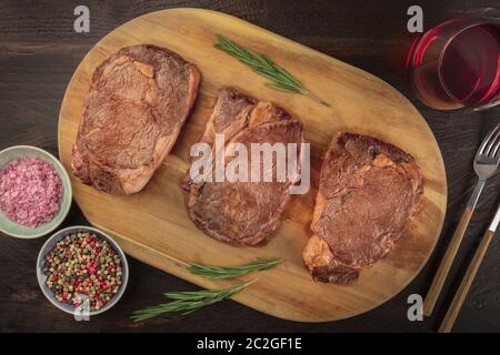Rinderfilet Steaks, Schuß von der Oberseite in einem dunklen Holzmöbeln im Landhausstil Hintergrund mit Rosmarin, Salz, Pfeffer, und Wein Stockfoto