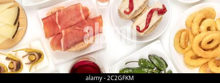 Ein Panorama von spanischen Tapas. Jamon, Tintenfischringe, Käse, gildas und andere Snacks, Schuß von oben auf weißem Hintergrund Stockfoto