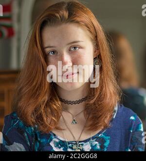 Indoor Portrait eines hübschen Teenage rothaarigen Weibliches mit Blaugrüne Augen und helles Gesicht und ein geschlossener Mund Grinsen trägt eine Choker Halskette und eine blaue Stockfoto