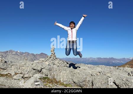 Eine junge Frau springt in die Luft in den Bergen und lacht vor Freude. Stockfoto