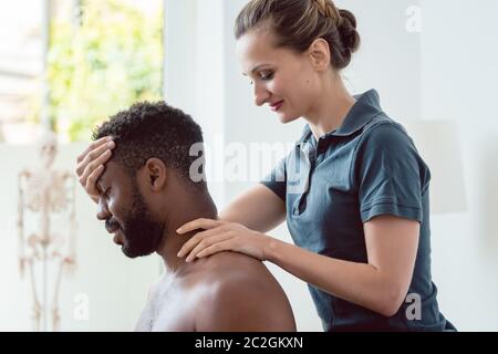 Frau Physiotherapeutin massiert jungen schwarzen Mann mit dem Kopf Stockfoto