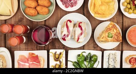 Ein Panorama spanischer Tapas. Wein, Jamon, Gazpacho, Tortilla und andere Snacks, von oben auf einem dunklen rustikalen Holzhinterholz geschossen Stockfoto