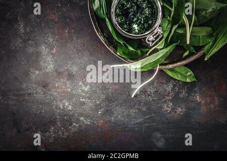 Frische Bärlauch-Blätter mit Pesto auf schwarzem Hintergrund. Wilder Lauch. Draufsicht. Freier Speicherplatz für Ihren Text. Stockfoto