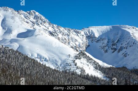 Die majestätischen schneebedeckten Hänge der Rocky Mountains in Colorado. Berge mit Schnee bedeckt und von Wald umgeben. Stockfoto