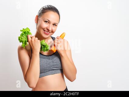 Schlanke junge Frau mit einer schönen Figur hält Gemüse in den Händen - Karotten und Salat Stockfoto