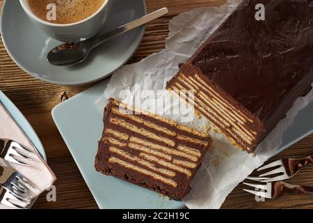 Schokoladenkuchen mit Schichten von Keksen, auf weissem Papier über blau Keramik Tablett serviert, mit Tasse cremigen Kaffee und Gabeln. Nahaufnahme von einem Stockfoto