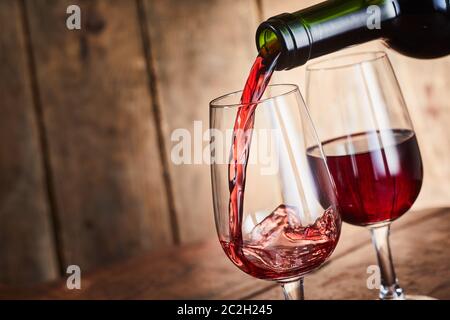 Gießen zwei Gläser von befestigten roten Portwein aus einer Flasche in einer Nahaufnahme geneigten Winkel Blick über Holz in eine Taverne mit Kopie Raum Stockfoto