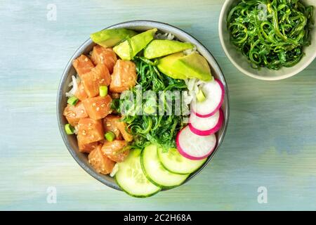 Eine Schüssel mit Lachs poke mit Avocado, Wakame und Gurke, Schuß von oben auf eine hellblaue Hintergrund Stockfoto
