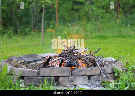 In einem runden Ziegelkamin brennen die Äste in einem Lagerfeuer Stockfoto