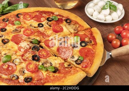 Pepperoni Pizza mit Salami Scheiben, schwarzen Oliven, Pilzen, frischen Basilikumblättern und viel Käse, auf einem dunklen rustikalen Holzbac Stockfoto