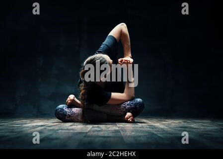 Junge Frau tut Yoga Padmasana Pose Variation auf dunklen Raum Stockfoto