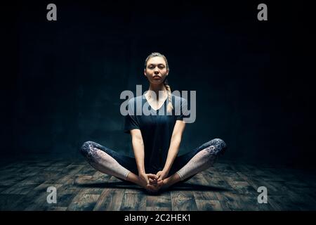 Junge Frau, die Yoga praktiziert, posiert auf dunklem Raum Stockfoto