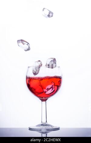 Eiswürfel fällt in ein Glas mit roter Flüssigkeit. Stockfoto