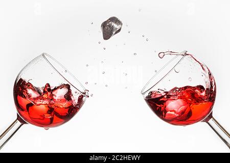 Eiswürfel fällt in ein Glas mit roter Flüssigkeit. Stockfoto