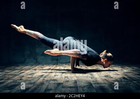 Junge Frau praktiziert Yoga dabei Hurdler Pose in dunklen Raum Stockfoto