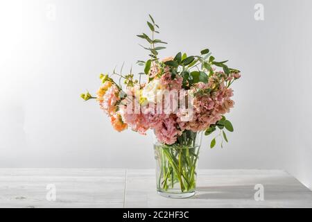 Ein Hochzeitsstrauß aus rosa und orange Lisianthus, antirrhinum und verschiedenen Sorten von Eukalyptus in einer Glasvase auf dem Küchentisch. Leerzeichen für Text Stockfoto