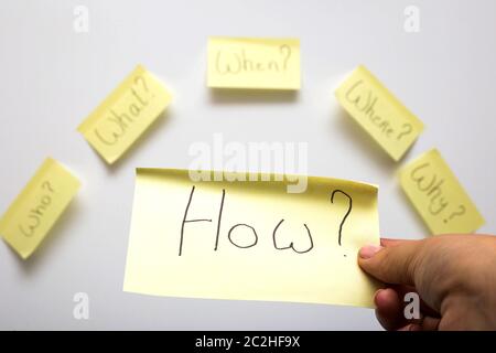 Die 6 Ws wer, was, wann, wo, warum, wie Frage auf sechs Haftnotizen auf strukturierte Schreibtisch Holz auf weißem Hintergrund closeup isoliert Stockfoto