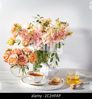 Hochzeitsstrauß aus rosa und orange Lisianthus, antirrhinum und Eukalyptus in Glasvase auf Küchentisch. Schwarzer Tee in einer weißen Tasse, Honigglas und Löffel Stockfoto