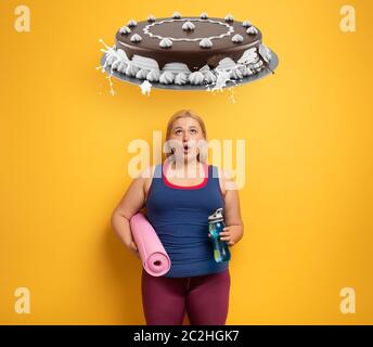 Fat Mädchen denkt, Süßigkeiten zu essen, anstatt zu tun Fitness-Studio. Gelber Hintergrund Stockfoto