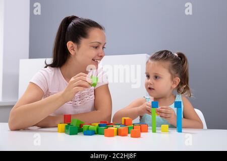 Lächelnd Kindertagesstätte Arbeitnehmer Spielen mit Kind Stapeln Bausteine auf weißem Schreibtisch Stockfoto