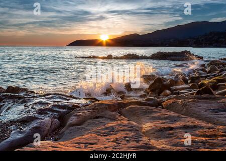 Sanremo Sonnenuntergang und Mittelmeer in Ligurien, Bezirk von Imperia. San Remo vom Strand. Küste Wellen spritzen und Sonne platzen. Italien Stockfoto