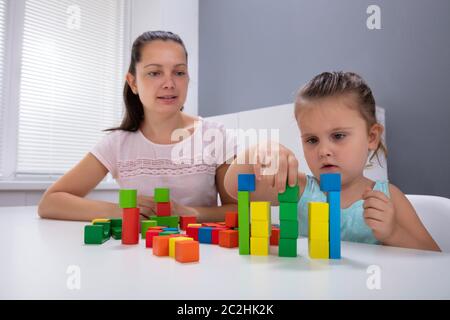 Lächelnd Kindertagesstätte Arbeitnehmer Spielen mit Kind Stapeln Bausteine auf weißem Schreibtisch Stockfoto