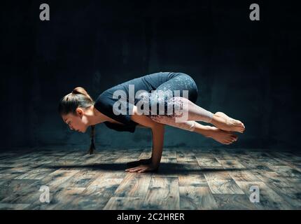 Junge attraktive Frau praktiziert Yoga tun Seite Kran Pose im dunklen Raum Stockfoto