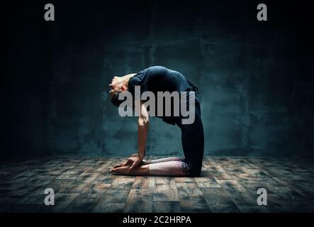 Junge Frau praktiziert Yoga tun Kamel Pose in dunklen Raum Stockfoto