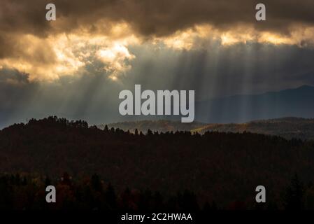 Dunkle Wolken und Sonnenstrahlen. Autumn Forest Hills in goldenen regnerischen Nachmittag. Stockfoto