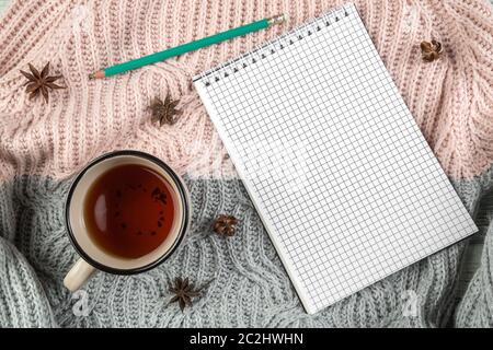 Gelbe Herbstblätter, eine Tasse Tee und ein Notizbuch auf einem strukturierten Pullover mit leerem Platz für Text. t Stockfoto