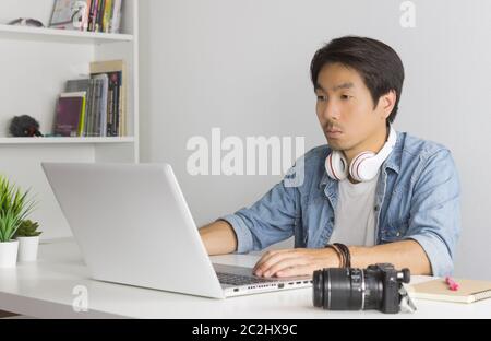 Asiatische freiberufliche Videofilmer in Denim oder Jeans Hemd bearbeiten Multimedia Datei per Laptop im Home Office. Freiberufliche Videofilmer arbeiten mit Technologie Stockfoto