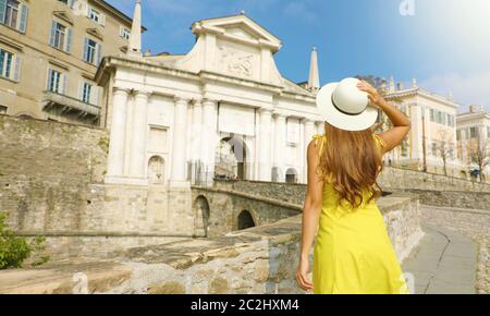 Schöne junge Frau mit Hut klettert in Richtung Porta San Giacomo Tor in Bergamo obere Stadt an einem sonnigen Tag. Sommer Urlaub in Italien. Stockfoto