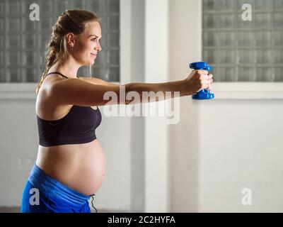 Schwangere Frau in ihren Dreißigern Training in einem Fitnessstudio tun Schulter Übungen mit Hanteln. Stockfoto