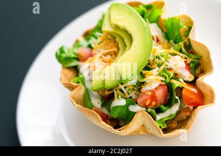 Ein Taco-Salat in Tortilla-Schüssel ist eine lustige und bunte Art, mexikanisches Essen zu essen. Mit frischen Zutaten wie Avocado, Tomaten, grünem Salat, Käse Stockfoto