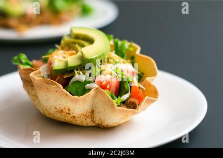 Ein Taco-Salat in Tortilla-Schüssel ist eine lustige und bunte Art, mexikanisches Essen zu essen. Mit frischen Zutaten wie Avocado, Tomaten, grünem Salat, Käse Stockfoto