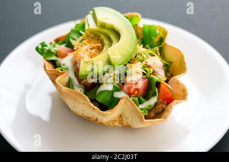 Ein Taco-Salat in Tortilla-Schüssel ist eine lustige und bunte Art, mexikanisches Essen zu essen. Mit frischen Zutaten wie Avocado, Tomaten, grünem Salat, Käse Stockfoto