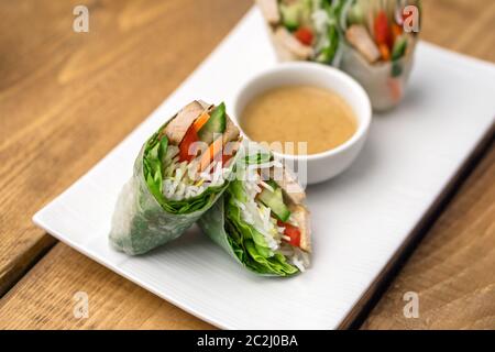 Frische vietnamesische Frühlingsrollen, ideal als gesunde Vorspeise mit Erdnussbutter-Sauce zum Eintauchen. Die Platte ist auf einem Holzhintergrund platziert. Stockfoto