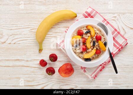 Haferbrei Haferbrei mit frischen Beeren und Obst in weißer Schüssel auf hellem Holzhintergrund. Draufsicht mit Kopierbereich. Konzept der gesunden Lebensweise, Gesundheit Stockfoto