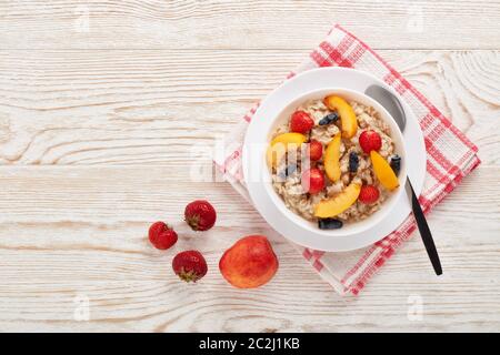 Haferbrei Haferbrei mit frischen Beeren und Obst in weißer Schüssel auf hellem Holzhintergrund. Draufsicht mit Kopierbereich. Konzept der gesunden Lebensweise, Gesundheit Stockfoto