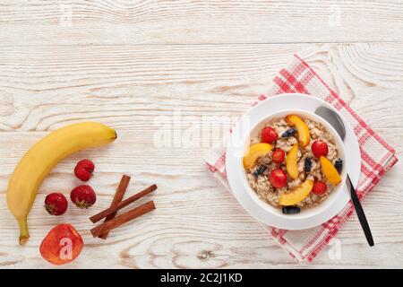 Haferbrei Haferbrei mit frischen Beeren und Obst in weißer Schüssel auf hellem Holzhintergrund. Draufsicht mit Kopierbereich. Konzept der gesunden Lebensweise, Gesundheit Stockfoto