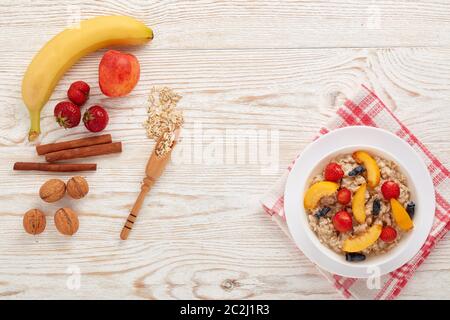 Haferbrei Haferbrei mit frischen Beeren und Obst in weißer Schüssel auf hellem Holzhintergrund. Draufsicht mit Kopierbereich. Konzept der gesunden Lebensweise, Gesundheit Stockfoto