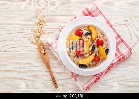 Haferbrei Haferbrei mit frischen Beeren und Obst in weißer Schüssel auf hellem Holzhintergrund. Draufsicht mit Kopierbereich. Konzept der gesunden Lebensweise, Gesundheit Stockfoto