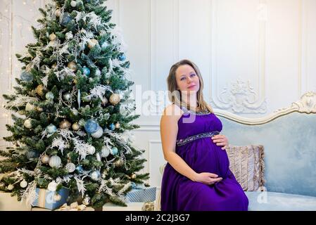 Schöne schwangere Frau in Ultra Violet Kleid auf dem Sofa sitzt. Stockfoto