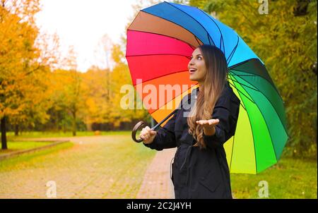 Fröhliche junge Frau mit bunten Regenschirm Kontrolle für Regen im City Park. Stockfoto