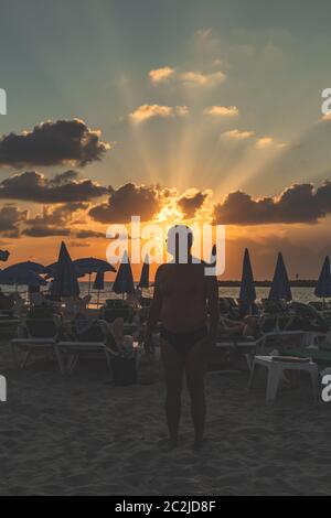 Silhouette eines Mannes, der am Abend kurz vor Sonnenuntergang unter den Sonnenliegen an einem Strand in Tel Aviv steht Stockfoto
