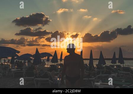 Silhouette eines Mannes, der am Abend kurz vor Sonnenuntergang unter den Sonnenliegen an einem Strand in Tel Aviv steht Stockfoto