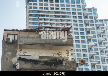 Foto eines alten baufälligen Hauses gegen ein neu errichtetes weißes mehrstöckiges Wohnhaus in der Hayarkon Street in Tel Aviv, Israel Stockfoto